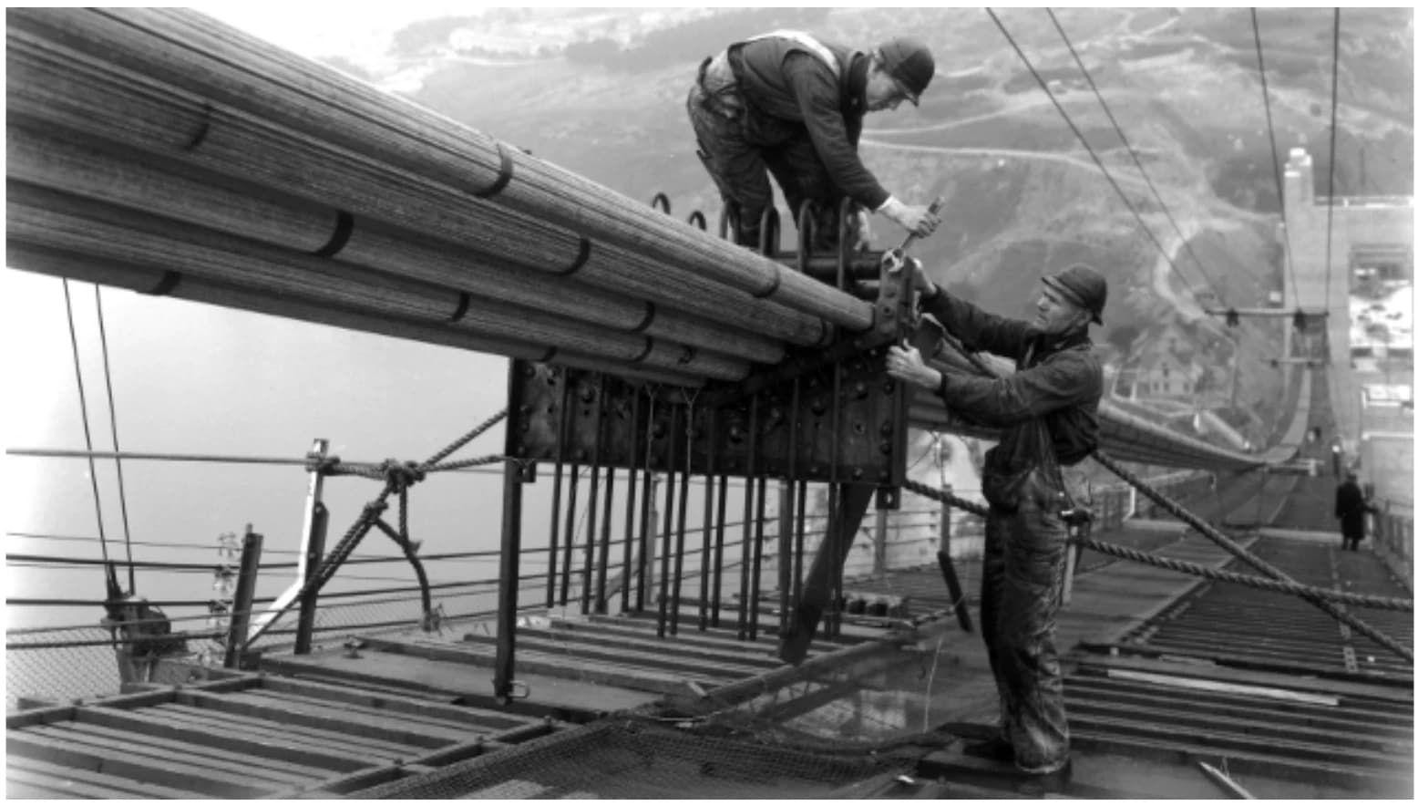 Two tradespeople working together on a suspension cable during construction of the Golden Gate Bridge.