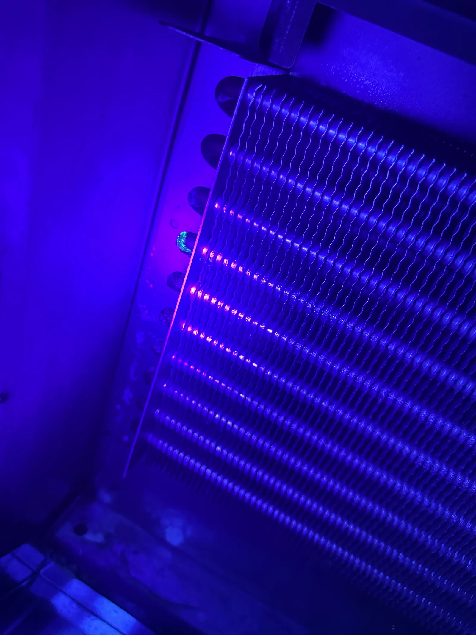 Evaporator coil under UV light with fluorescent dye glowing green at the leak point